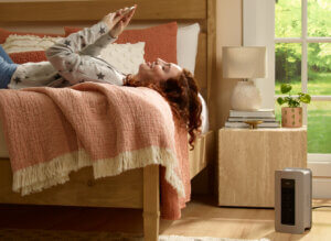 a woman lying on a bed looking at her phone while one of Honeywell's safe heaters warms the room.
