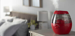 a red Honeywell humidifier on a bedside table humidifying a bedroom